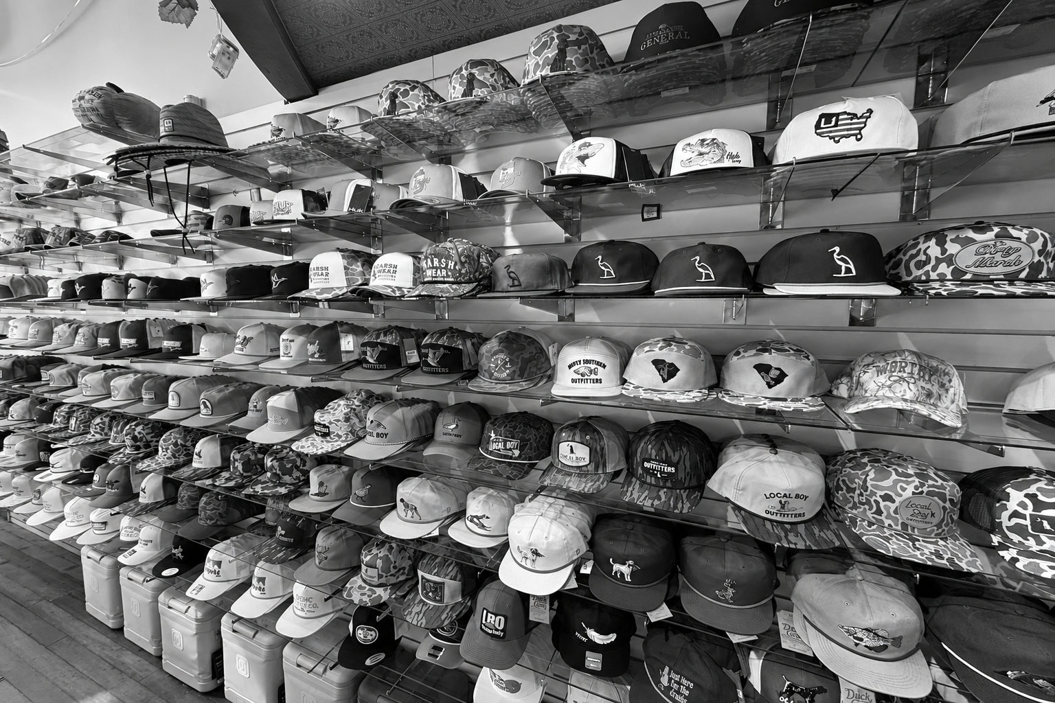 A retail display wall filled with many baseball caps in various colors, patterns, and sizes, photographed in a store interior with shelving and floor visible.